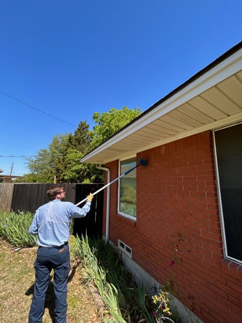 A Berrett Pest Control Denver technician using a pole to clean eaves of a house in Denver, CO.