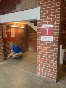 A pest control technician inspecting or treating the base of a brick wall in a commercial building by EcoPro Termite & Pest in Dayton, OH