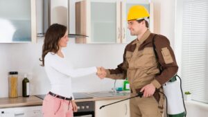 A pest control technician shaking hands with a customer in a kitchen, representing a service call by Aksarben Bat & Critter Removal in Omaha, NE