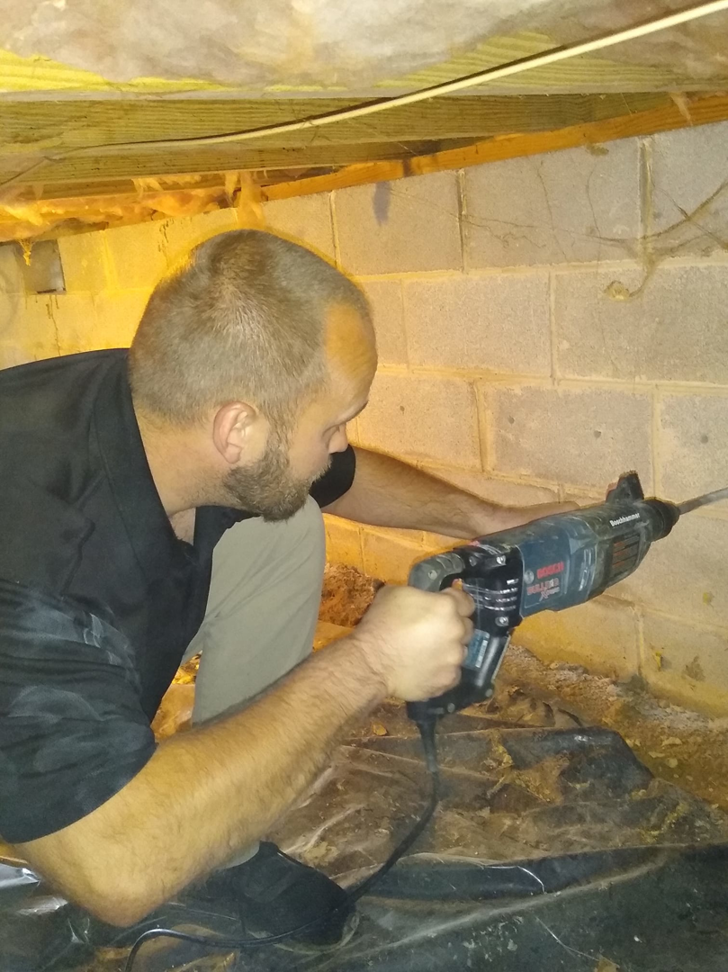 A pest control technician from Power Pest Solutions in Knoxville, TN, drilling into a foundation wall for termite treatment.