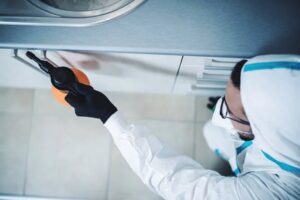 A pest control technician in a protective suit applying treatment in a kitchen cabinet for Brownco Pest Control in Wilmington, DE.