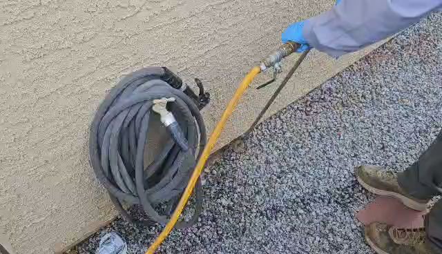 A pest control technician's gloved hand holding a spray hose for treatment at Bye Bye Bugs Pest Control in Indianapolis, IN