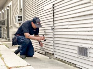 A pest control technician from Aantex Pest Control Norcal inspecting the base of a building in Sacramento, CA.