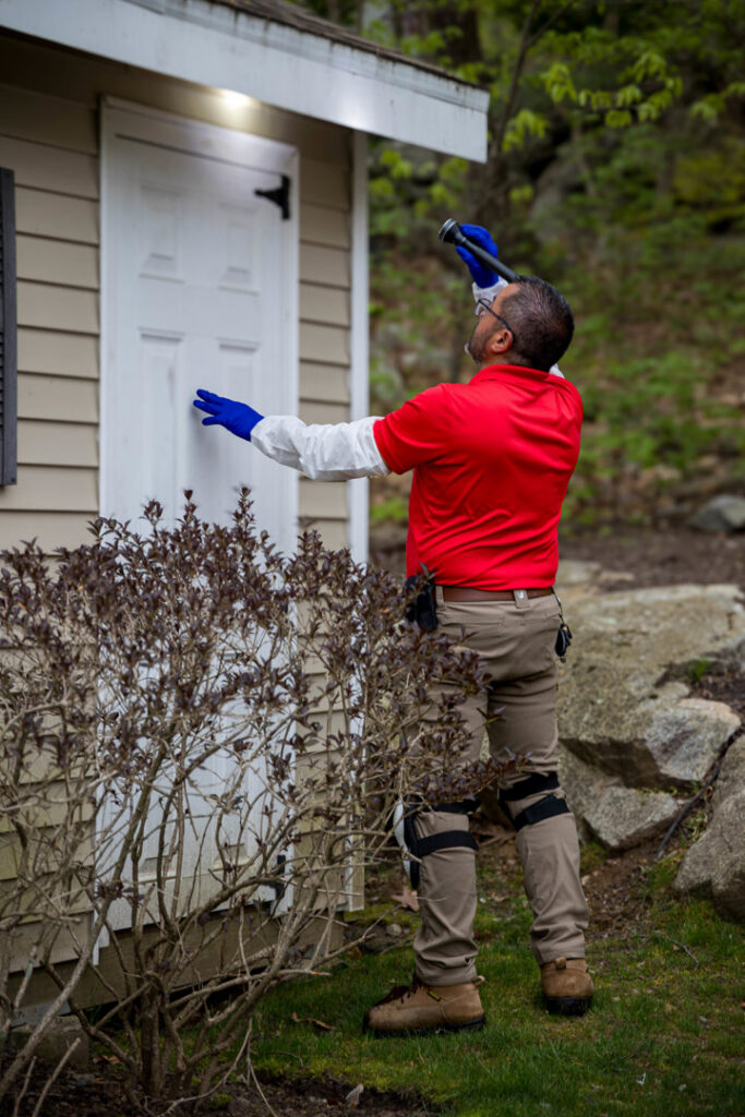 A pest control technician inspecting the exterior of a building for pests at Big Blue Bug Solutions in Providence, RI
