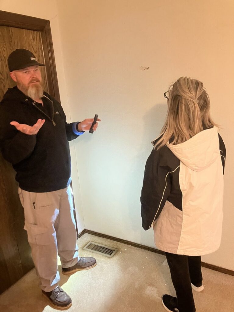 An Absolute Pest Solutions technician inspecting a home with a flashlight and consulting a client in Piedmont, OK.