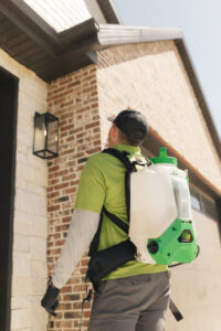 A pest control technician inspecting the eaves of a house with a backpack sprayer at Pure Pest Solutions in North Ogden, UT.