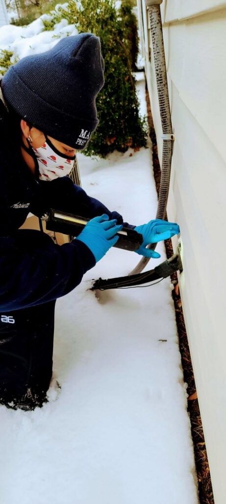 A Mario's Pest Control technician inspecting the exterior of a house for pests in the snow in Hamilton, NJ.