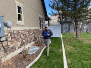 A pest control technician inspecting the house perimeter for pests at a client's home by All Green Pest Control and Lawn Care in Provo, UT.