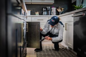 A Fox Pest Control technician inspecting a kitchen cabinet for pests with a flashlight in Glen Ellyn, IL