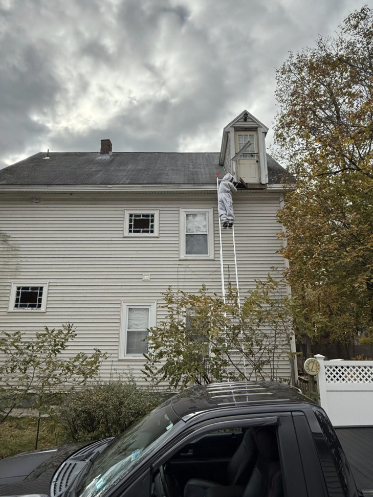 A pest control technician in a protective suit on a ladder working on a house for Squish in Manchester, NH.