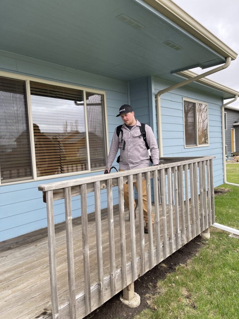 A pest control technician walking on a residential deck with a backpack sprayer for Defend Pest Solutions in Sioux Falls, SD.
