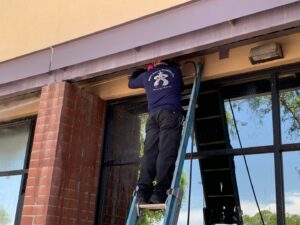 A pest control technician on a ladder working on a commercial building, providing services for Pigeon Control Phoenix AZ in Glendale, AZ.