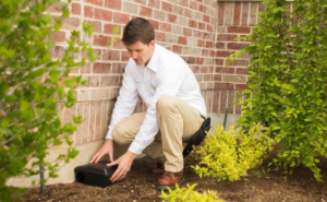 A pest control technician from EDGE - The Service Company placing a bait station near a home in Bridgeview, IL.