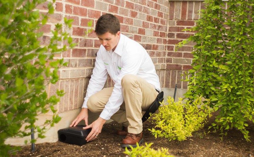 A pest control technician from EDGE - The Service Company placing a bait station near a home in Bridgeview, IL.