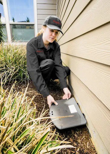 A pest control technician placing an exterior pest control bait station for X-Out Pests Control in Little Rock, AR.
