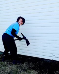 A Mario's Pest Control technician using a tool to prepare the ground for a pest treatment around a house foundation in Hamilton, NJ.