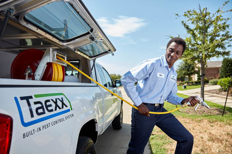 A HomeTeam Pest Defense technician preparing to spray, pulling a hose from a service truck in Longwood, FL.