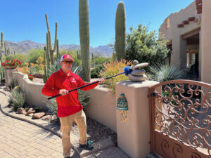 A pest control technician removing cobwebs from a gate post with a long duster by Overson Pest Control LLC in Mesa, AZ