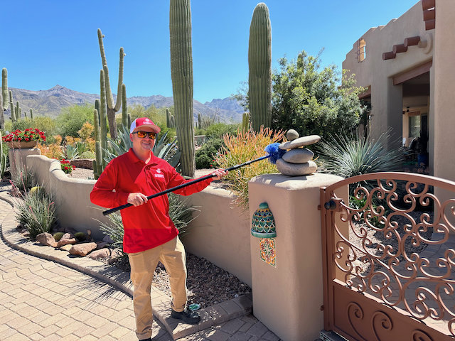 A pest control technician removing cobwebs from a gate post with a long duster by Overson Pest Control LLC in Mesa, AZ