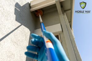 A pest control technician from The Noble Way Pest Control removing spider webs or nests from house eaves in Sacramento, CA.