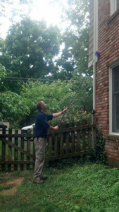 A pest control technician removing webs or nests from high on a house at Out A Site Pest Control in Cincinnati, OH