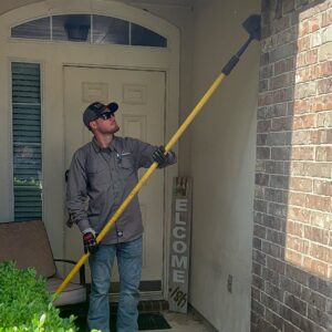 A pest control technician from Kaizen Pest Management removing spiderwebs from a house exterior in Austin, TX.
