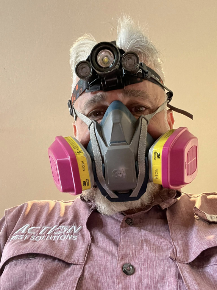 A pest control technician wearing a respirator mask and headlamp from Action Pest Solutions in Lowell, AR.