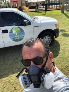 A pest control technician wearing a respirator mask with a Globe Pest Inc truck in the background in Miami, FL.