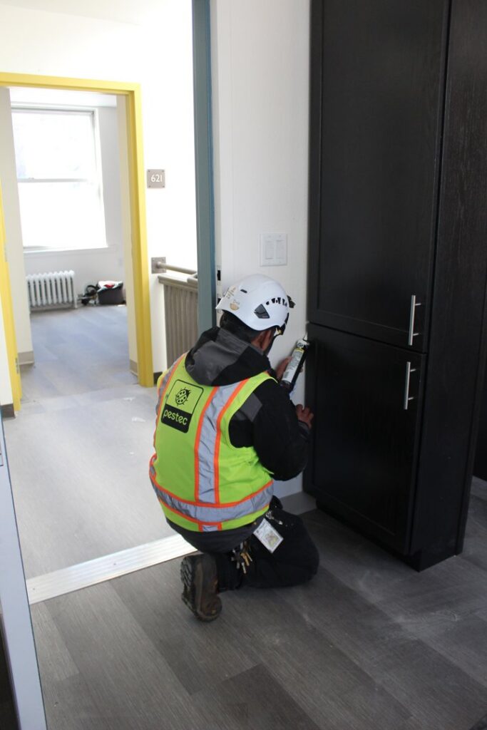 A Pestec technician sealing a potential pest entry point near a cabinet in San Francisco, CA.