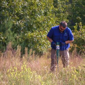 A pest control technician setting a bait station in a grassy field for 1st Choice Pest Solutions in Eau Claire, WI.