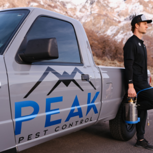 A Peak Pest Control technician holding a sprayer next to a branded truck, ready for a pest control job in Ogden, UT.