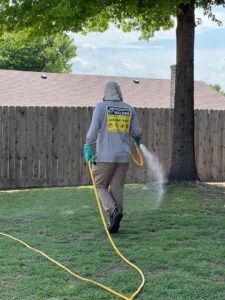A Mosquito Malone Pest Control technician spraying a backyard lawn for pest treatment in Edmond, OK.