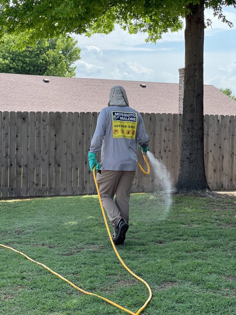 A Mosquito Malone Pest Control technician spraying a backyard lawn for pest treatment in Edmond, OK.