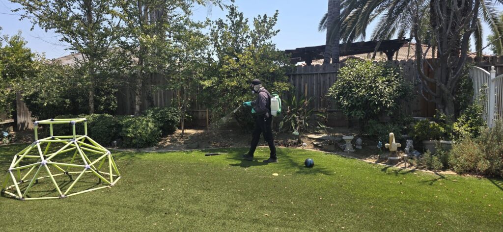 A Natrix Pest Control technician in Bakersfield, CA, applying pest treatment with a backpack sprayer in a residential backyard.