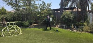 A Natrix Pest Control technician in Bakersfield, CA, applying pest treatment with a backpack sprayer in a residential backyard.