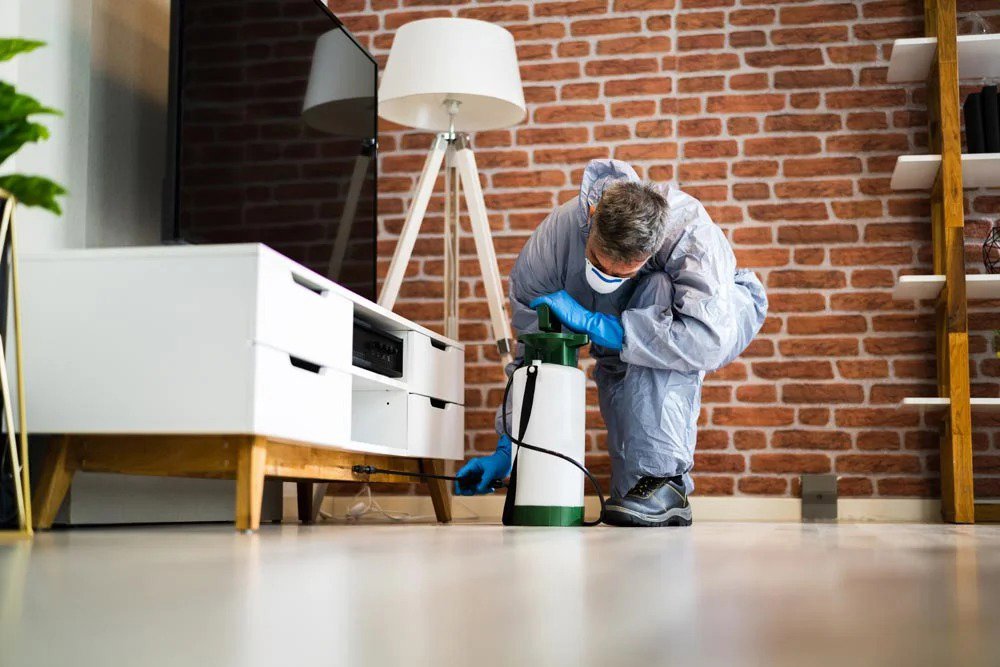 A pest control technician in a protective suit spraying along a baseboard for Venum Pest Solutions in Fayetteville, NC.