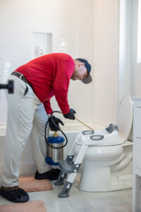 A pest control technician spraying around a toilet in a bathroom for indoor pest control by DOA Pest Service in Nashville, TN.