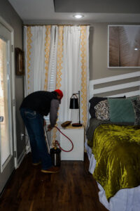A pest control technician from Liberty Pest Services LLC spraying behind a nightstand in a bedroom in Mayflower, AR.