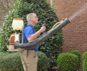 A Pest Magic Pest Control technician spraying bushes near a house with a backpack sprayer in Forsyth, GA.