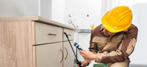 A pest control technician spraying under a kitchen cabinet at a job site for One Stop Termite & Pest Control in Memphis, TN.