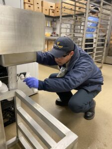 A Crazy Ant Pest Control technician spraying under equipment in a commercial kitchen in Fresno, CA.