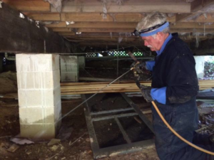 A pest control technician spraying pest treatment in a residential crawl space at All-Around Termite and Pest Control in Tallahassee, FL.