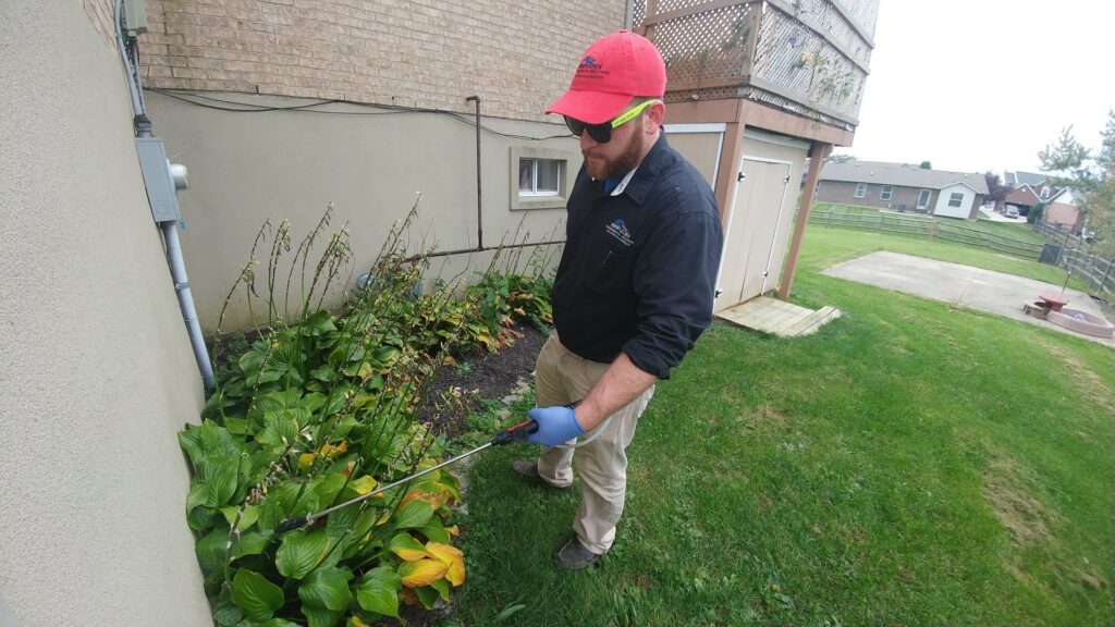 A pest control technician from Ampulex Environmental Solutions in Oxford, OH, spraying the exterior of a home for pests.