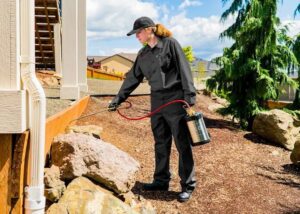 A pest control technician spraying pest control treatment along the exterior foundation for X-Out Pests Control in Little Rock, AR.