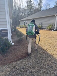A Port City Pest Control technician applying pest treatment to the exterior foundation of a house in Summerville, SC.