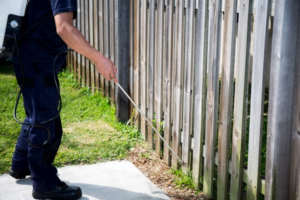 A pest control technician spraying along a wooden fence line for outdoor pest control by Rocky Mountain Pest Control in Santa Fe, NM.