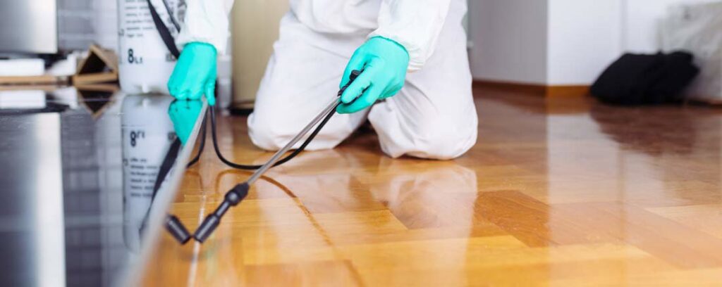 A pest control technician in protective gear spraying a floor for pests by Frost Integrated Pest Management in Portland, OR.