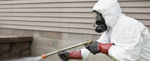 A pest control technician in a protective suit spraying a building foundation for RNR Pest Services in Atlanta, GA.