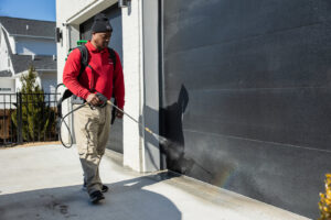 A pest control technician spraying the exterior of a garage door for pest treatment by DOA Pest Service in Nashville, TN.