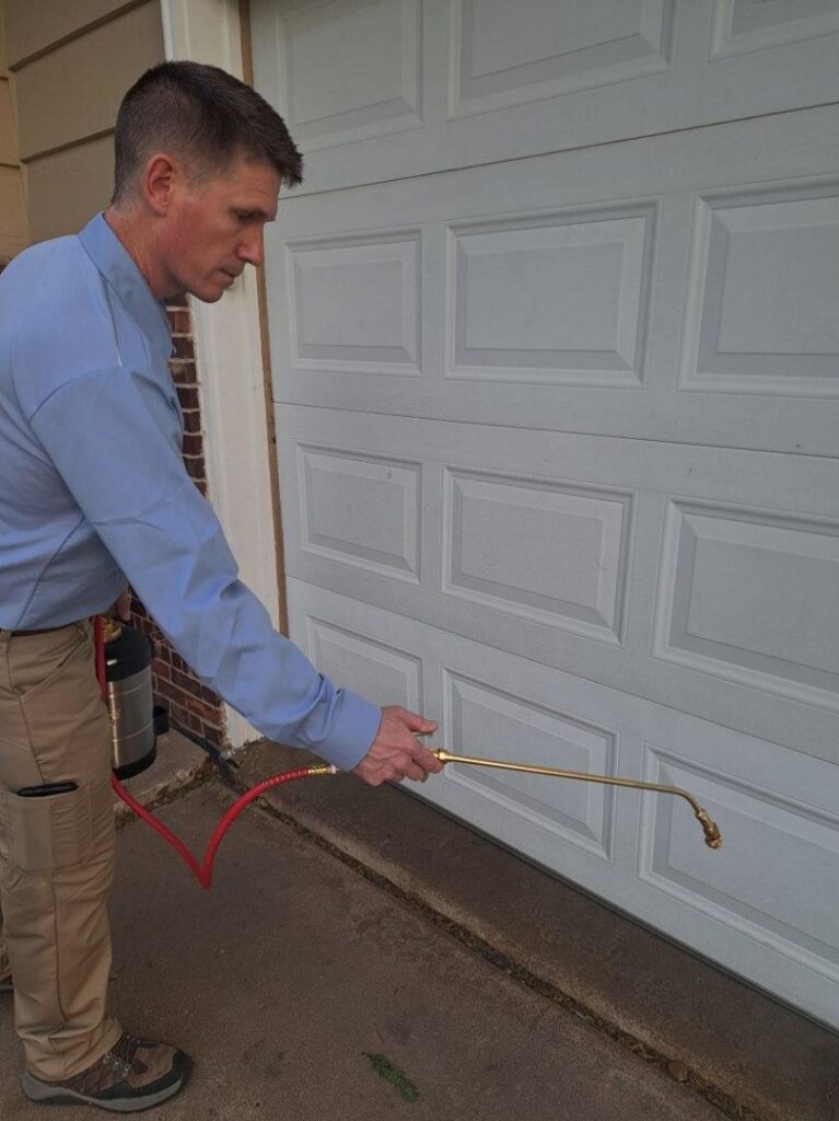 A Howe Pest Management technician in Manhattan, KS, applying pest control treatment to the base of a garage door.